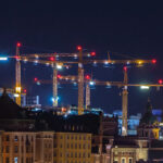 Upplysta byggkranar över centrala Stockholm. Natthimmel och ljus som speglas i fjärdens mörka vatten. Vi söker en kommunikatör som får platsen att tala.